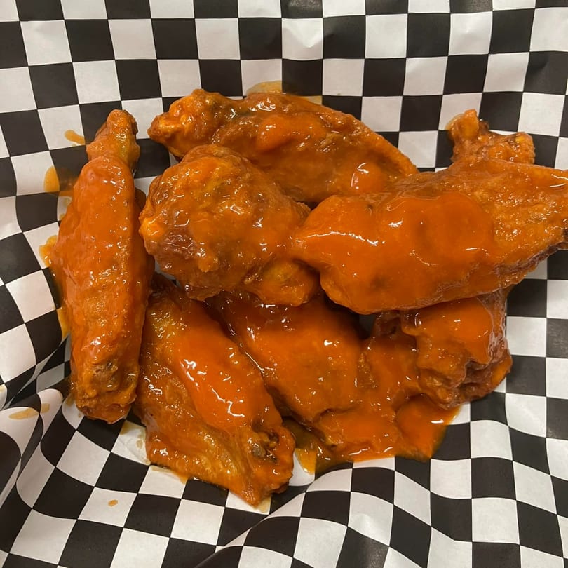 Buffalo wings from Jordan's Hot Dogs & Mac, coated in bright orange sauce on checkered paper.